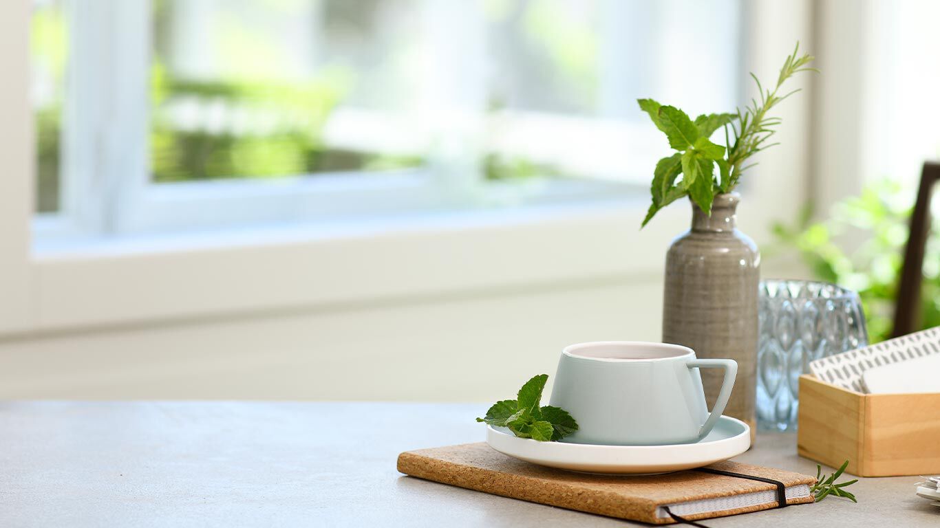 Une tasse de th&eacute; est pos&eacute;e sur une table blanche, &agrave; c&ocirc;t&eacute; d&rsquo;un vase.